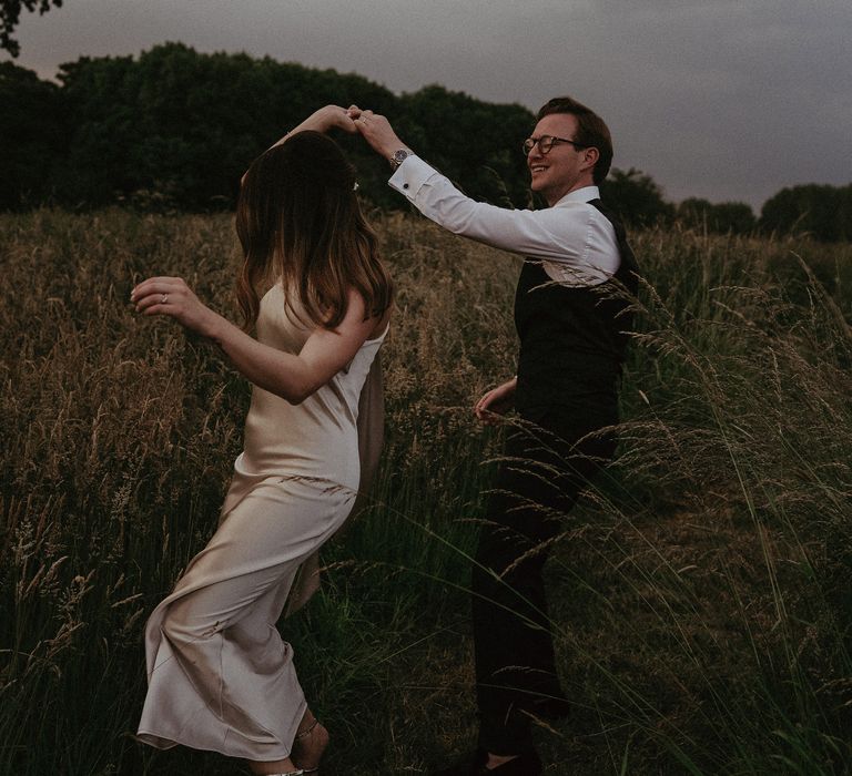 Groom twirls bride around outdoors in the countryside on their wedding day