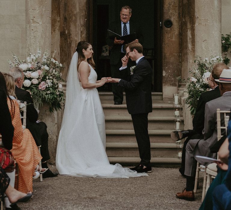 Bride & groom stand in front of staircase leading to large door at Elmore Court on the day of their wedding