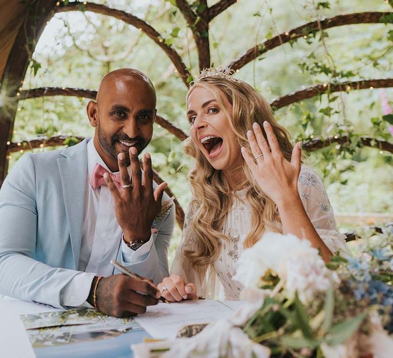 Bride & groom sign wedding papers after ceremony as they show off their wedding rings