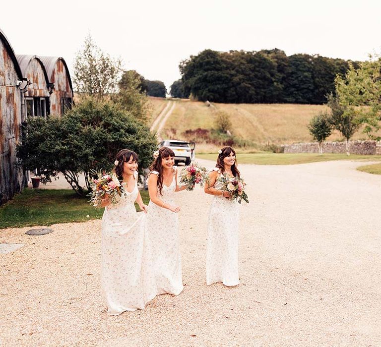 Bridesmaids wear floral bridesmaids dresses and hold colourful bouquets complete with green foliage and bright flowers