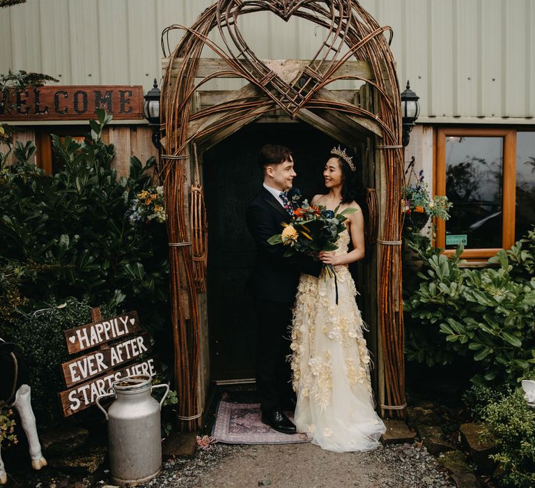 Groom in dark suit stands in doorway with bride in strapless feathered wedding dress and headpiece for Wellbeing Farm wedding in Lancashire 