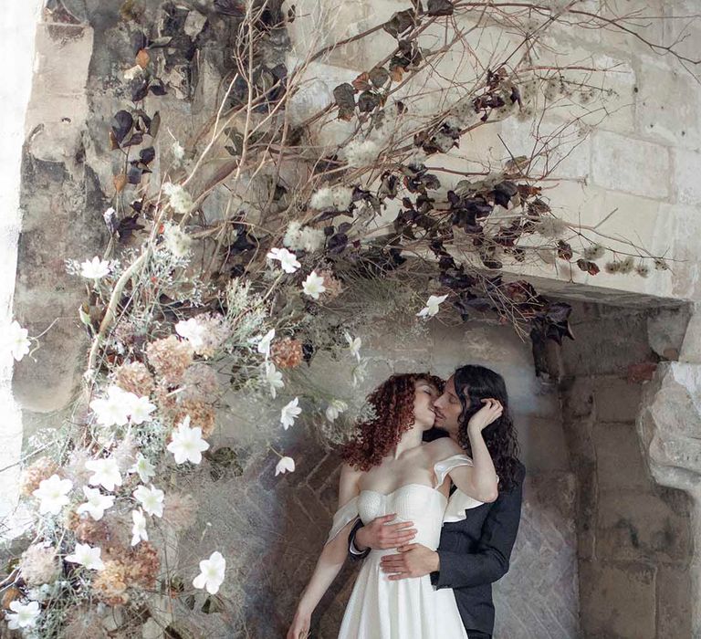 modern gothic wedding inspiration at Blackfriars Priory with bride in a strapless wedding dress kissing her groom in a black suit in a giant fireplace 