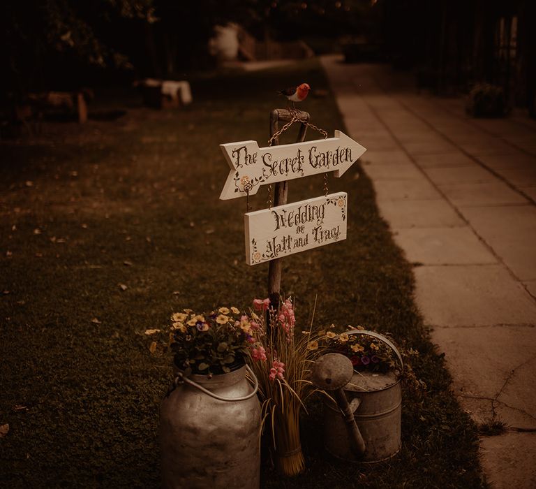 The secret garden wedding sign with tin watering cans filled with flowers 