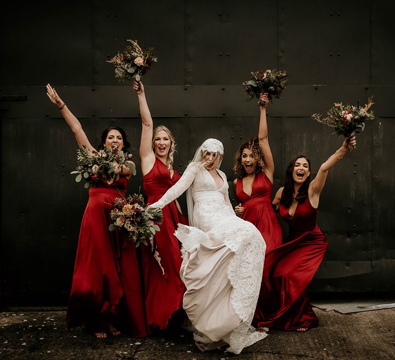 Bridal party portrait with bride in a lace wedding dress and bridesmaids in red satin bridesmaid dresses 