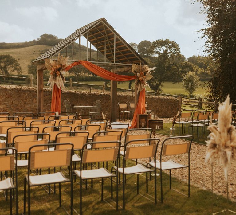 Outdoor wedding ceremony at farm in Dorset with orange draping and pampas grass installations