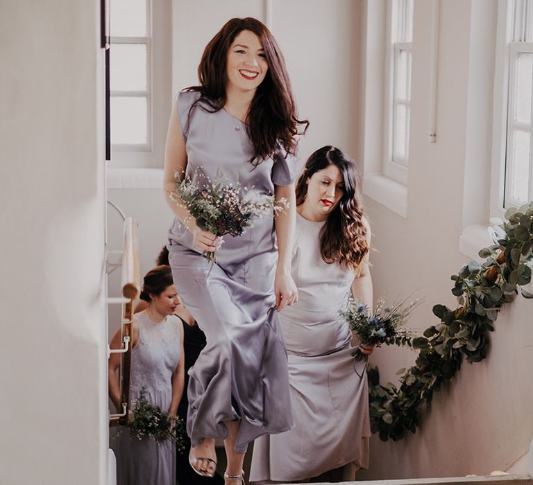 Bridesmaids walk up staircase wearing lavender gowns 