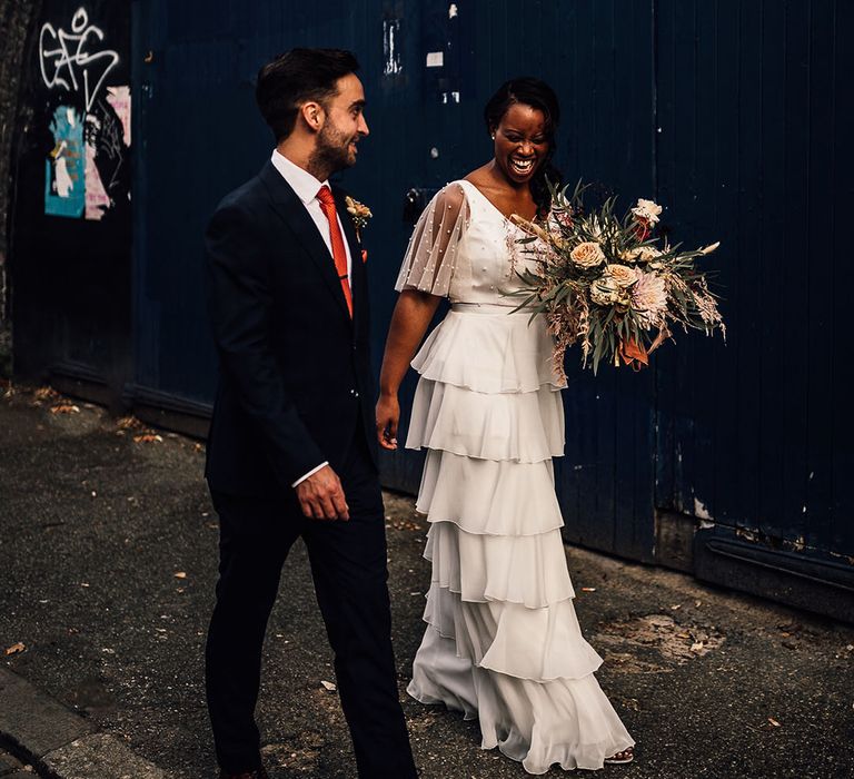 Urban bride and groom portrait in London with Black bride in a layered tulle wedding dress and groom in a navy blue suit 