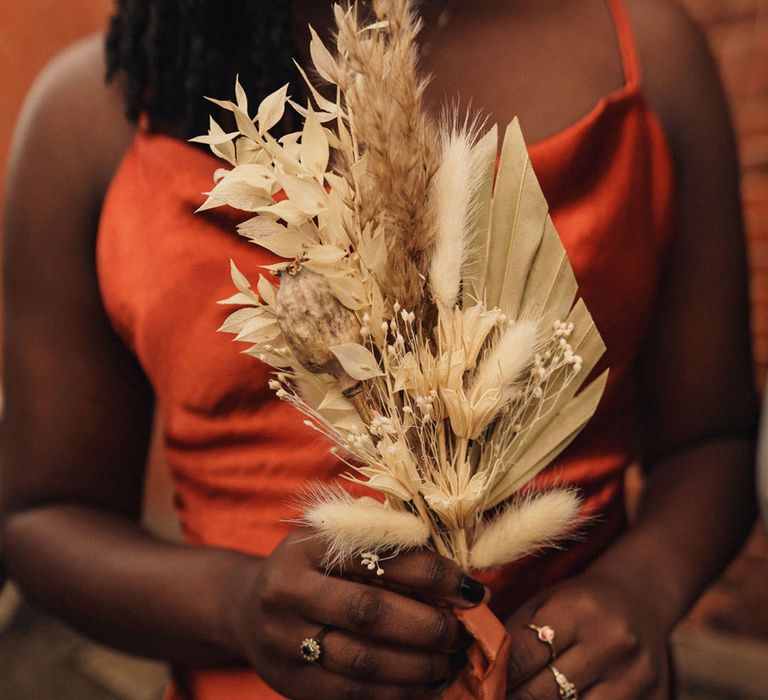 Bridesmaid holds dried floral bouquet complete with pampas grass whilst wearing burnt orange gown