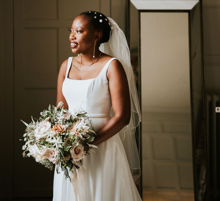 Pearl hair accessory on bride in square neckline wedding dress and gold pearl drop earrings 