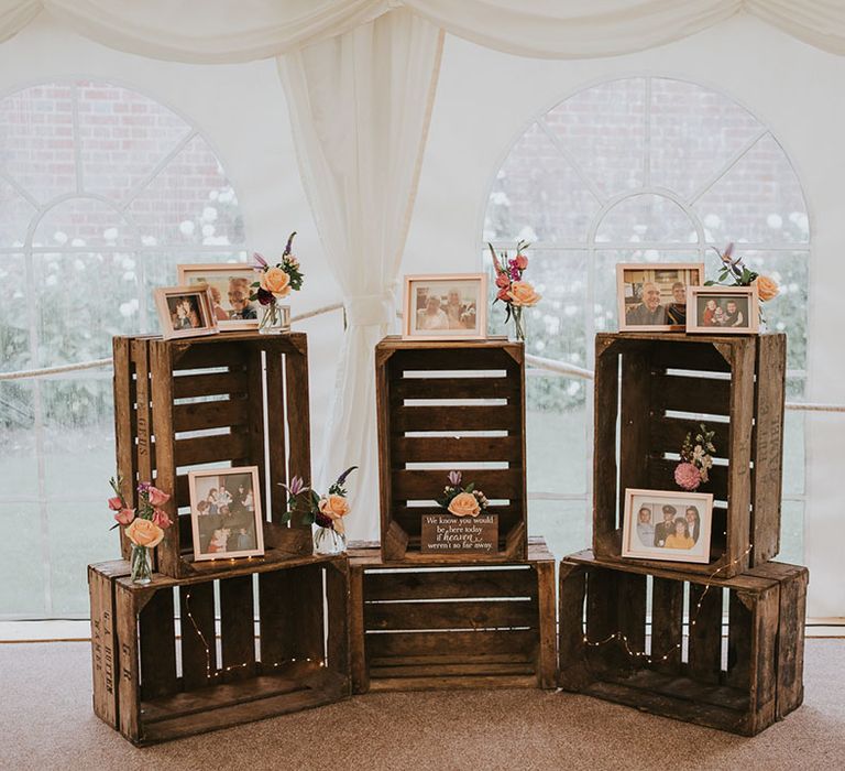 Area of wooden crates with family photos of late family members with fairy lights, decorative wooden plaque and flowers