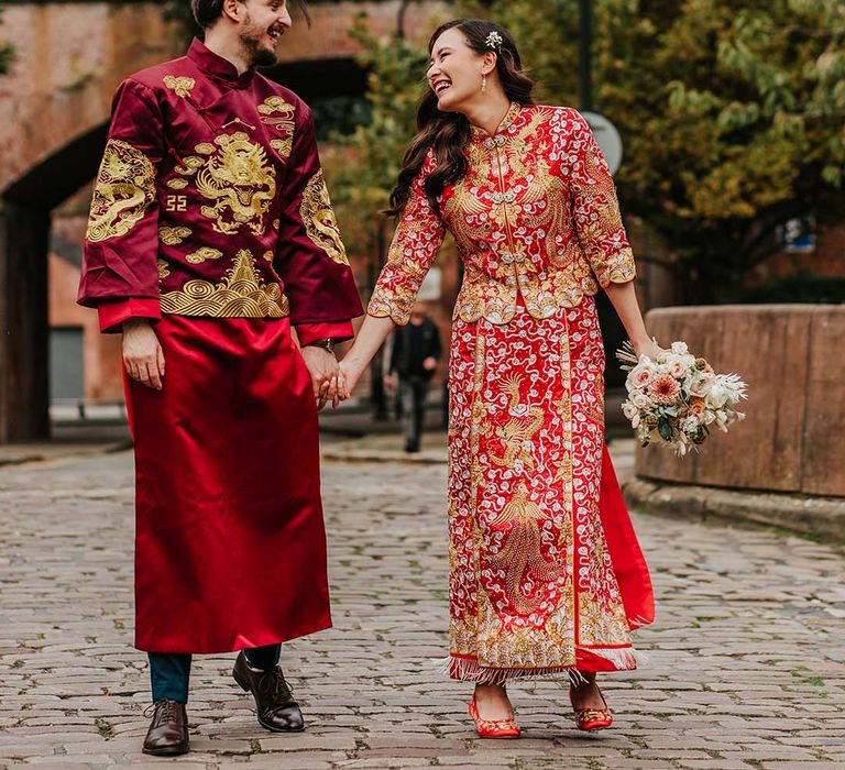 Bride and groom laugh with ecah other as they walk the streets of Manchester in traditional red and gold Chinese wedding attire