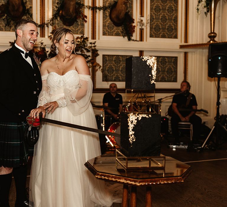 Bride and groom cut their two tier black wedding cake with gold flakes with a sword 