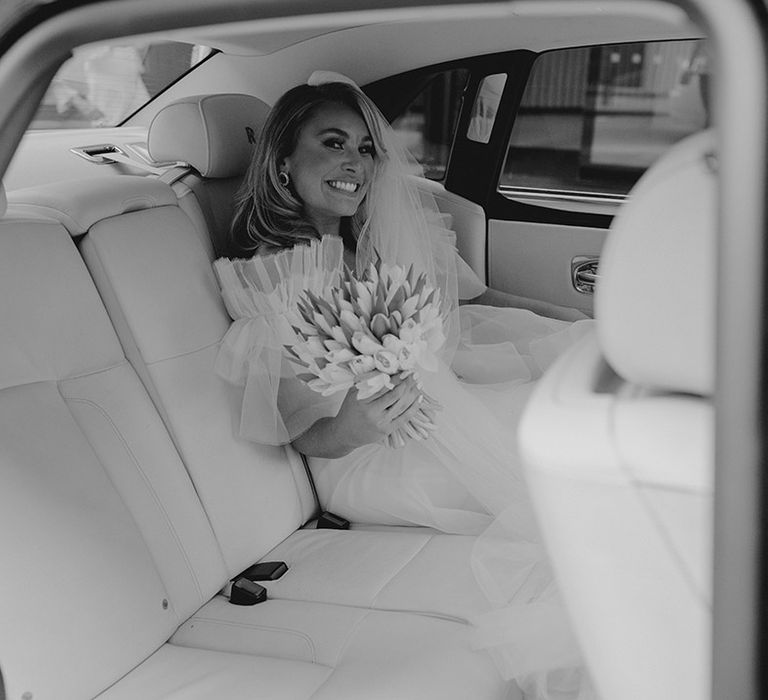 Bride in ruffle Halfpenny London wedding dress holding white tulip bouquet in wedding car