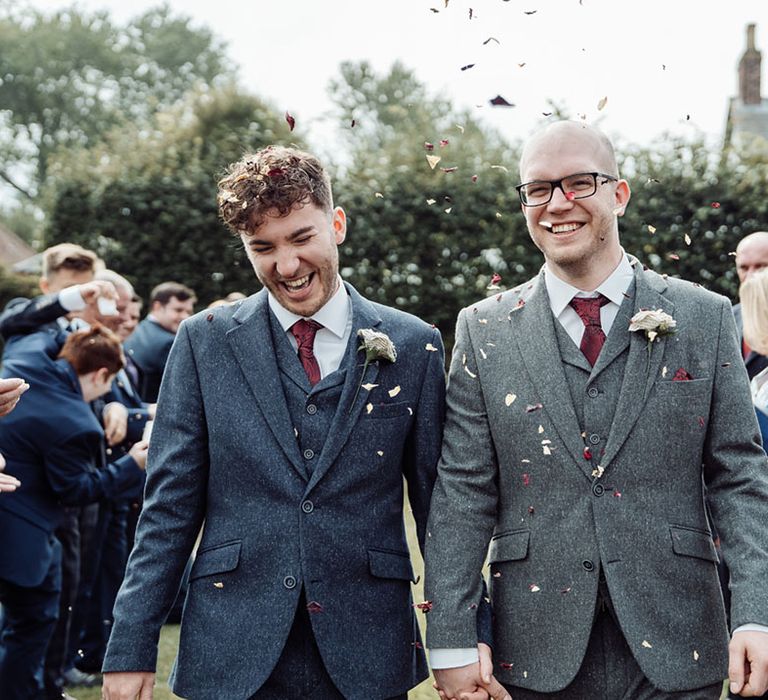 Grooms in green and dark blue three piece suits for their barn wedding having their confetti exit from their ceremony