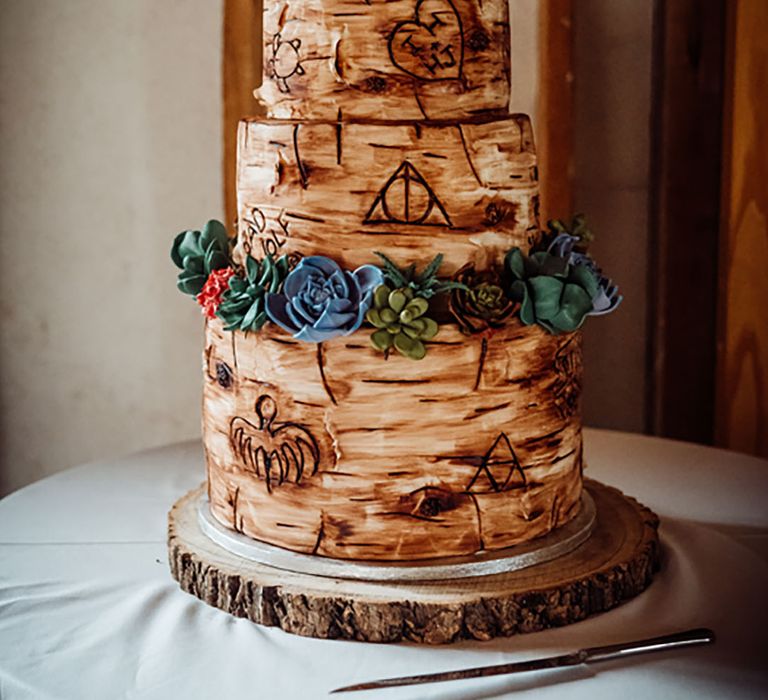 Three tier wedding cake with tree trunk style icing with sentimental carvings and colourful flowers with wooden initial cake topper 