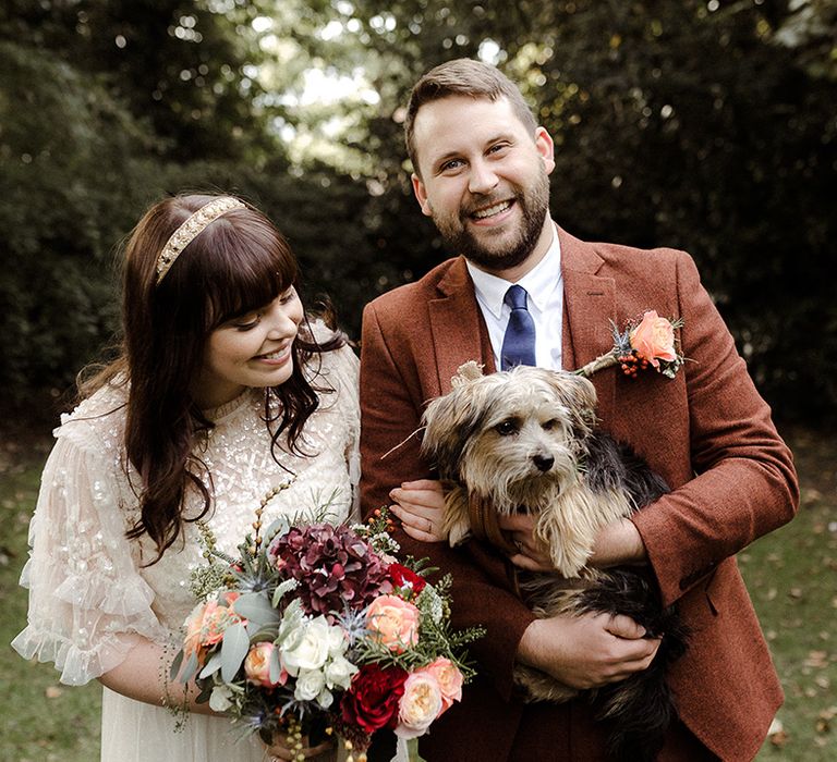 Bride links arms with the groom as he holds their cute pet dog 