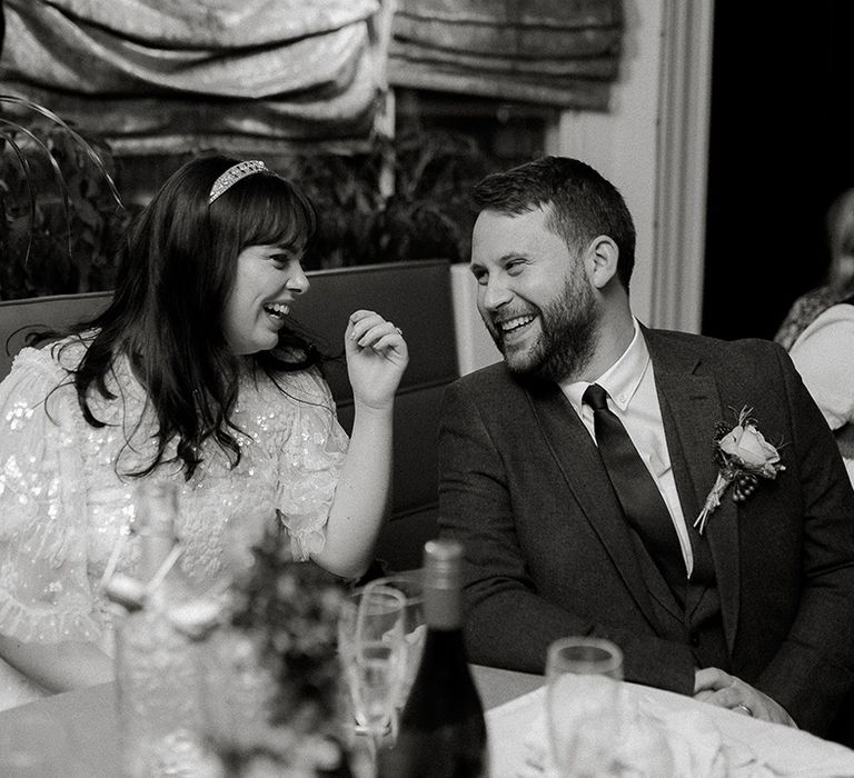 Bride and groom laugh together at their wedding reception during speeches