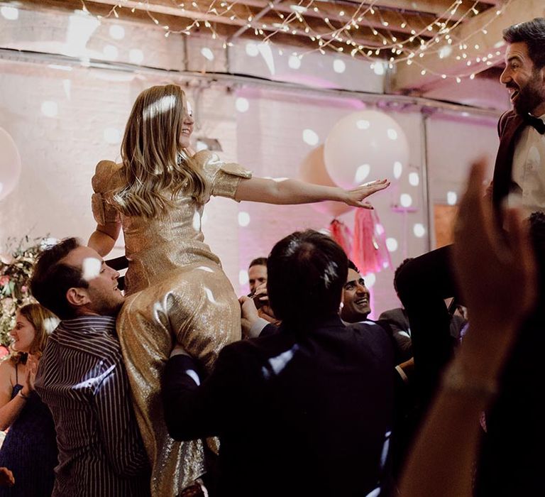 Bride and groom are lifted up on chairs for wedding reception with fairy lights and white balloon decoration 