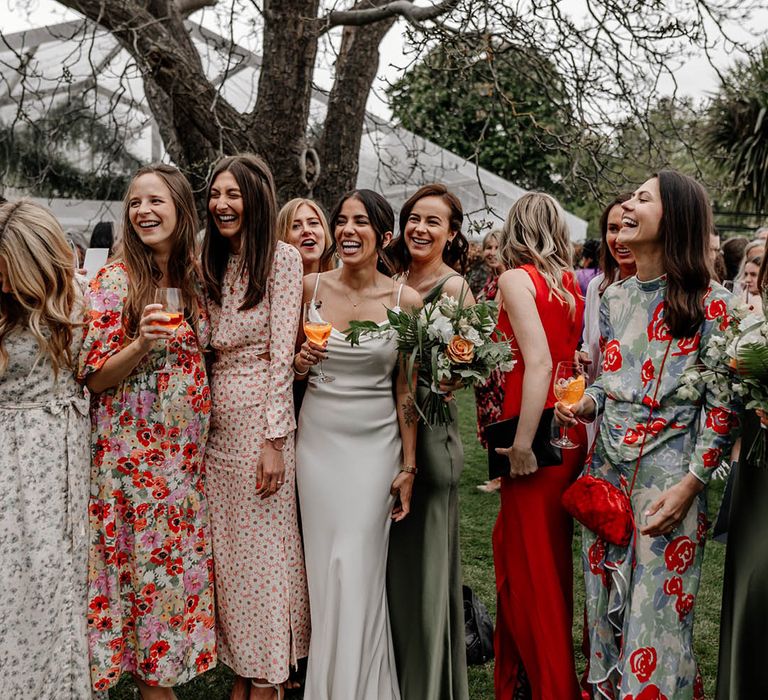 Bride in a white satin wedding dress laughing with her friends at her back garden wedding 