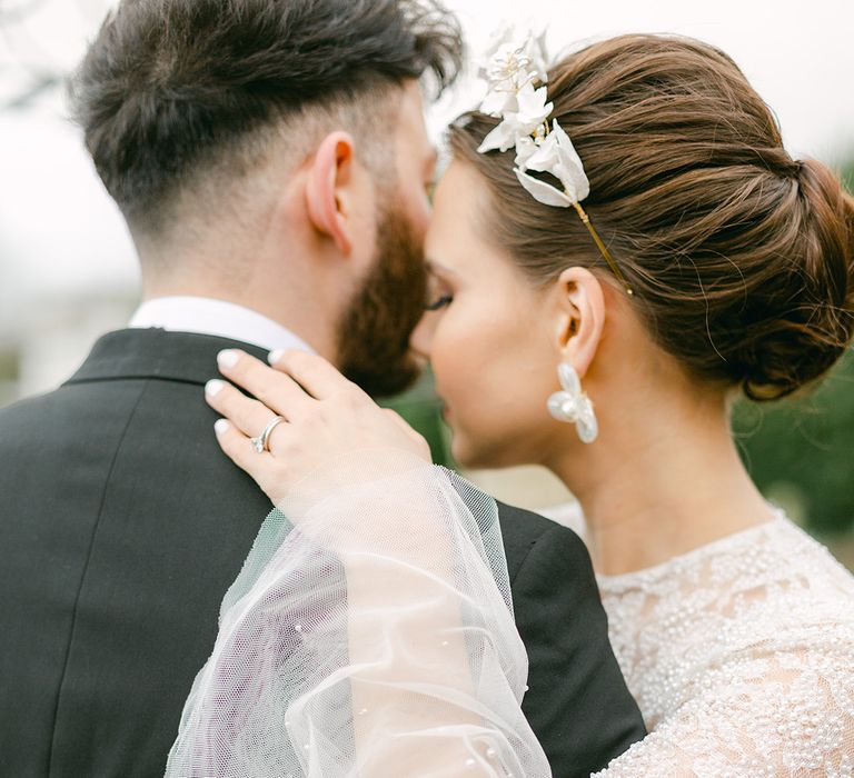 Bride in a beaded wedding dress with fluted sleeves embracing her groom in a tuxedo 