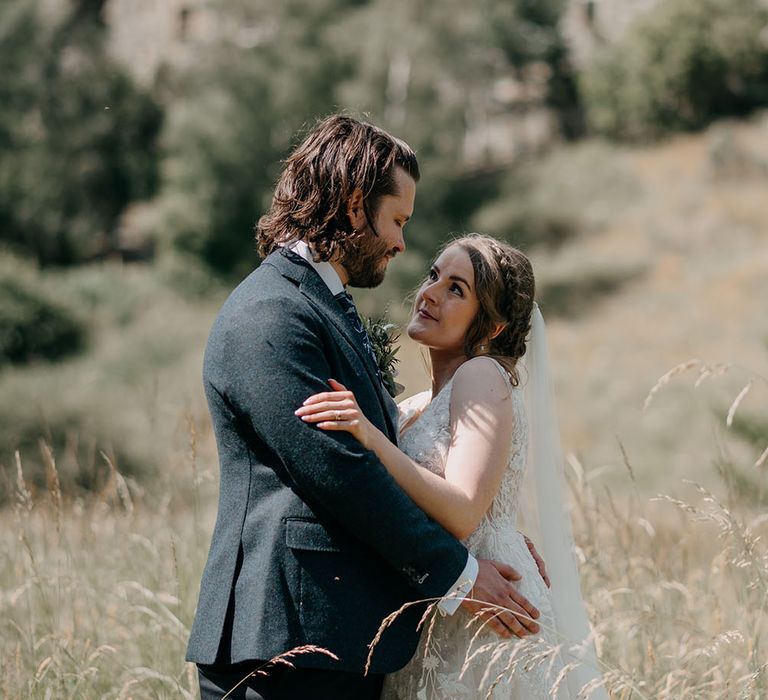 Bride looks lovingly at her groom outdoors in Scotland with Neidpath Castle to the background and greenery surrounding them