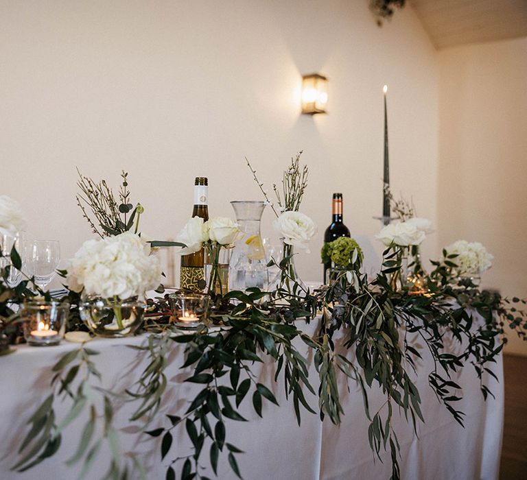 White flower and green foliage top table with tall dark green taper candles 