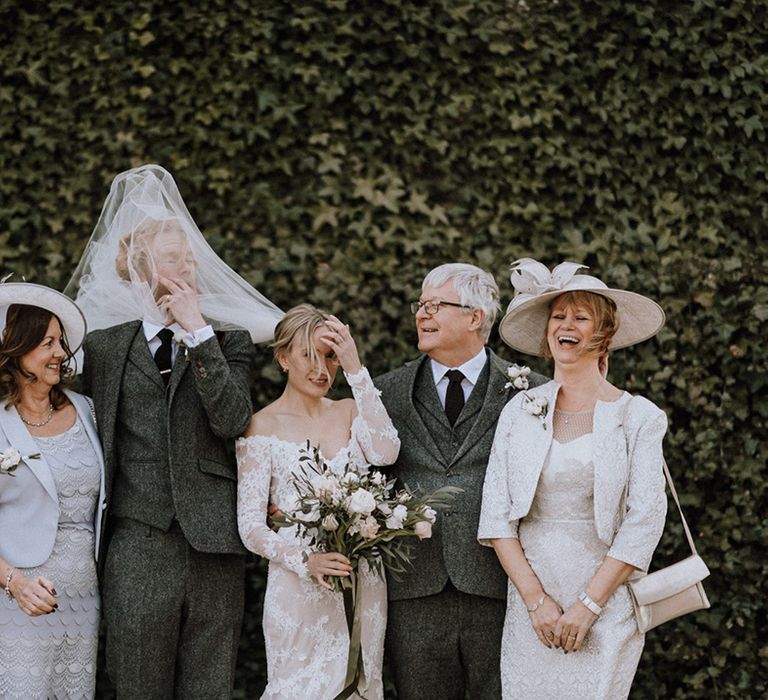 Bride's veil blows in the grooms face as they take pictures with their parents on a windy wedding day 