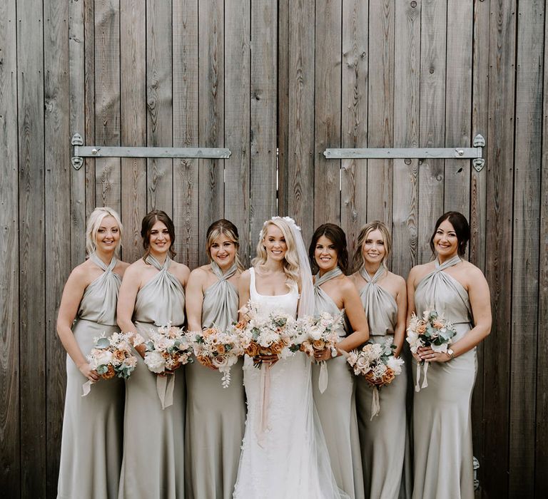 Bridal party with bridesmaids in halter neck sage green satin bridesmaid dresses with the bride in a floral wedding dress 