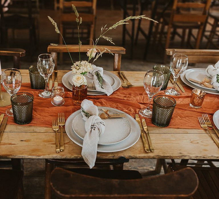 Orange table runner with gold cutlery, coloured glassware and plain plates for the table settings 