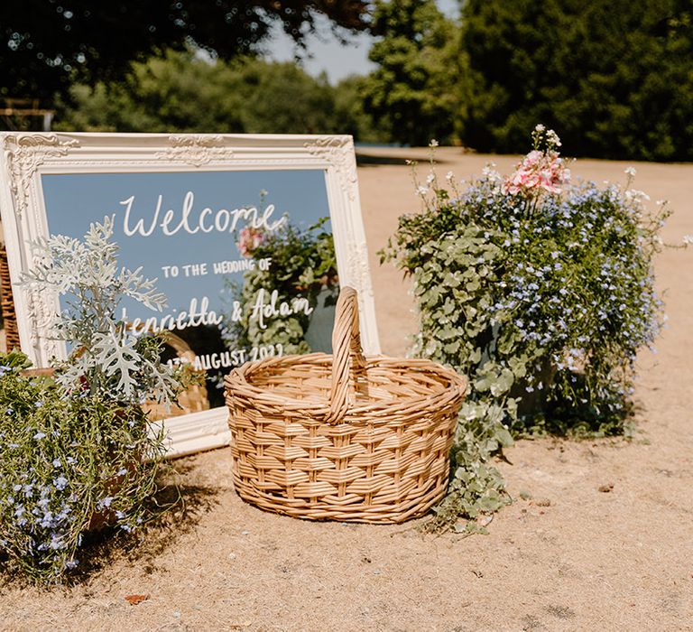 White framed mirror with white writing and wicker basket surrounded by floral bouquets