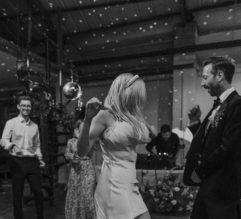 Bride in short white satin dress with feather trimmed neckline dancing with groom in dark tux and bowtie at stylish modern London wedding