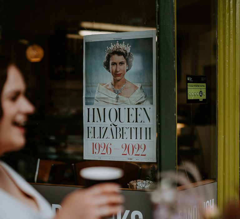 Bride drinks pint at pub wedding venue in London with a poster of Queen Elizabeth II in the background