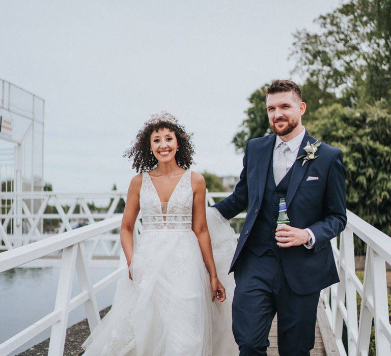 Curly haired bride in boho Maggie Soterro wedding dress walks alongside her groom before Thames boat ride 