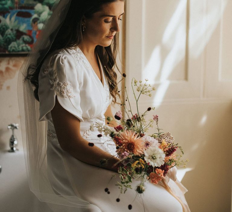 Bride sitting in handmade embroidered wedding dress holding rustic wedding flowers bouquet 