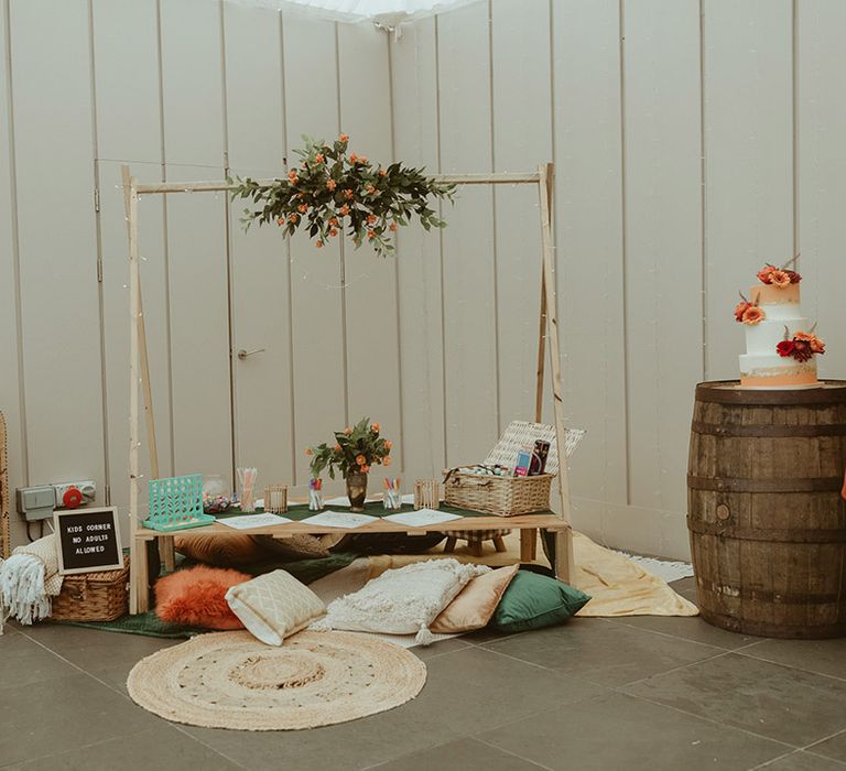 Kid's station with blankets, colouring, pretzel bar next to the three tier orange and white iced wedding cake autumn wedding