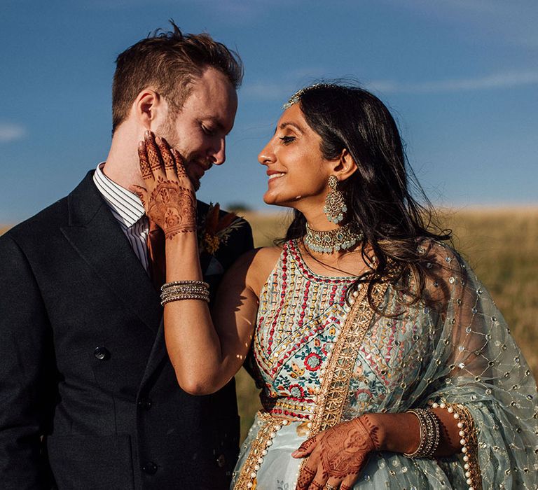 Indian bride wears statement earrings and colourful lehenga as she looks lovingly toward her groom during golden hour portraits 