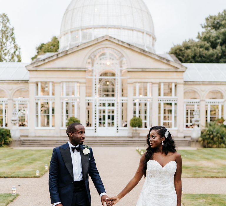 Black bride in strapless sweetheart wedding dress walking with the groom in a blue tuxedo for traditional Catholic wedding 