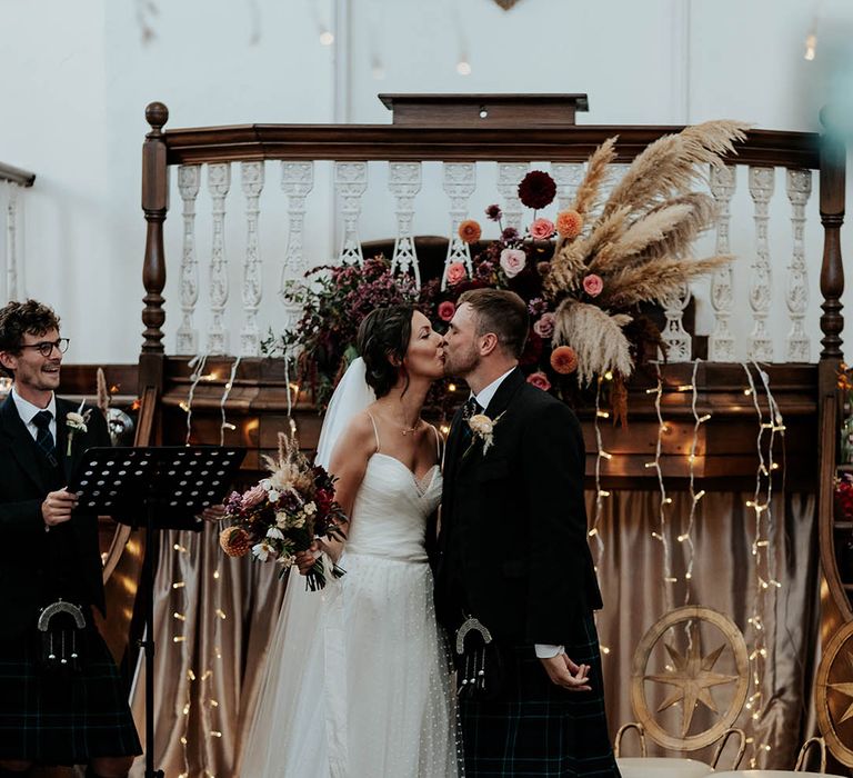 Bespoke wedding ceremony with fabric wedding sign, pampas grass, fairy light decor, a groom in a kilt and a bride in a polka dot Stephanie Allin bridal gown