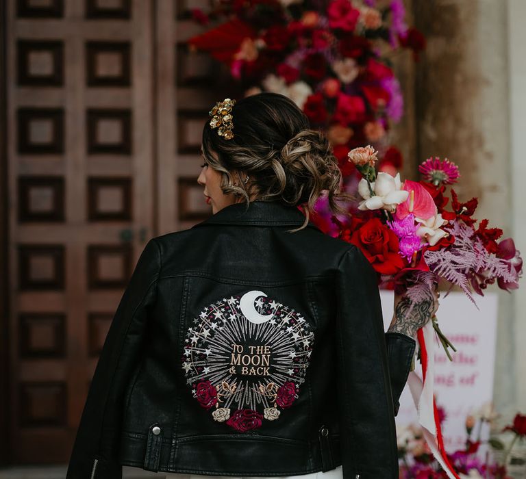 To The Moon and Back bridal leather jacket with bright pink and red wedding bouquet held by the bride