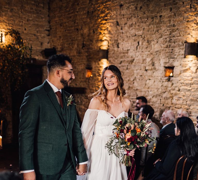 Bride in long balloon sleeve wedding dress walking with the groom back down the aisle as a married couple 