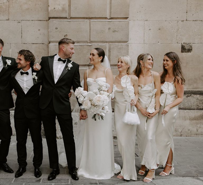 Black tie dress code for city wedding with the wedding party adhering to the dress options with black tuxedos and white satin bridesmaid dresses 