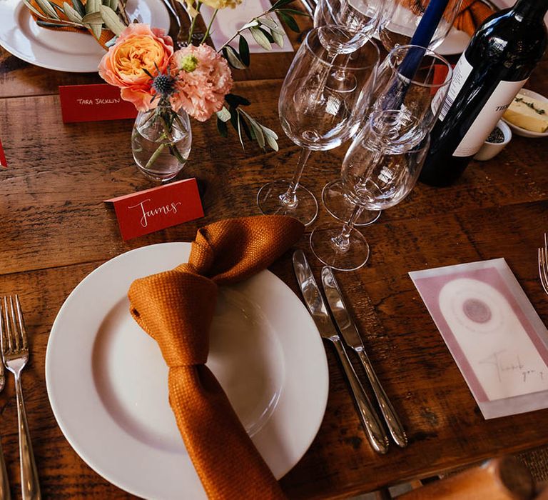 White wedding plate with copper orange napkin and place name with wedding favours in frosted envelopes 