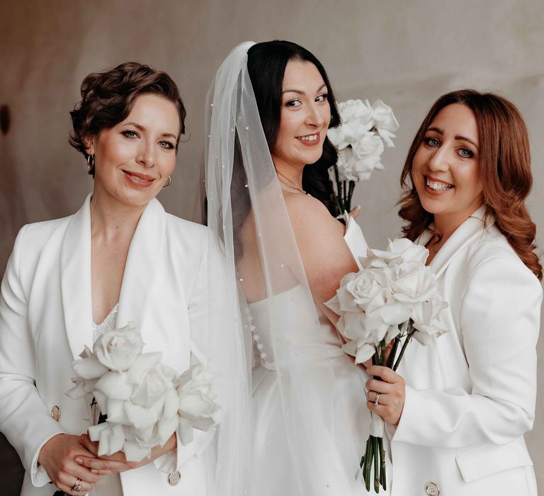 Bride with bridesmaids in white bridesmaid suits and white rose wedding bouquet