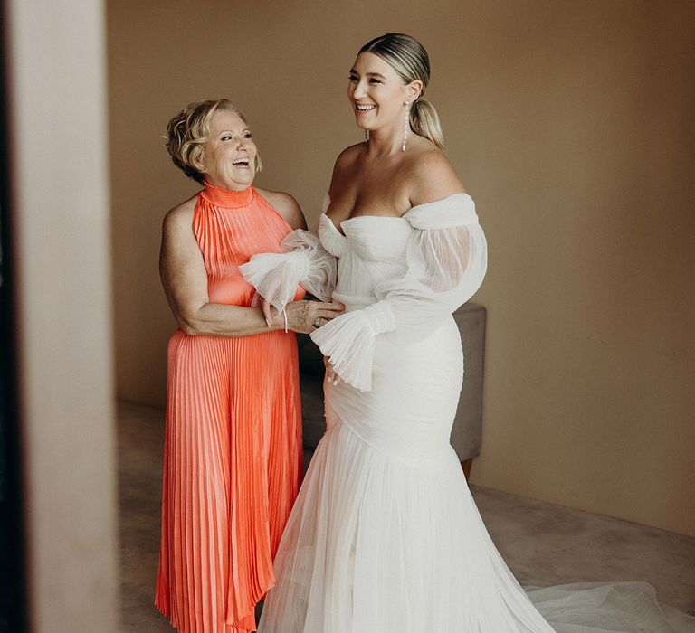 coral mother of the bride dress and bride in a strapless tulle wedding dress with sheer long sleeves on the wedding morning 