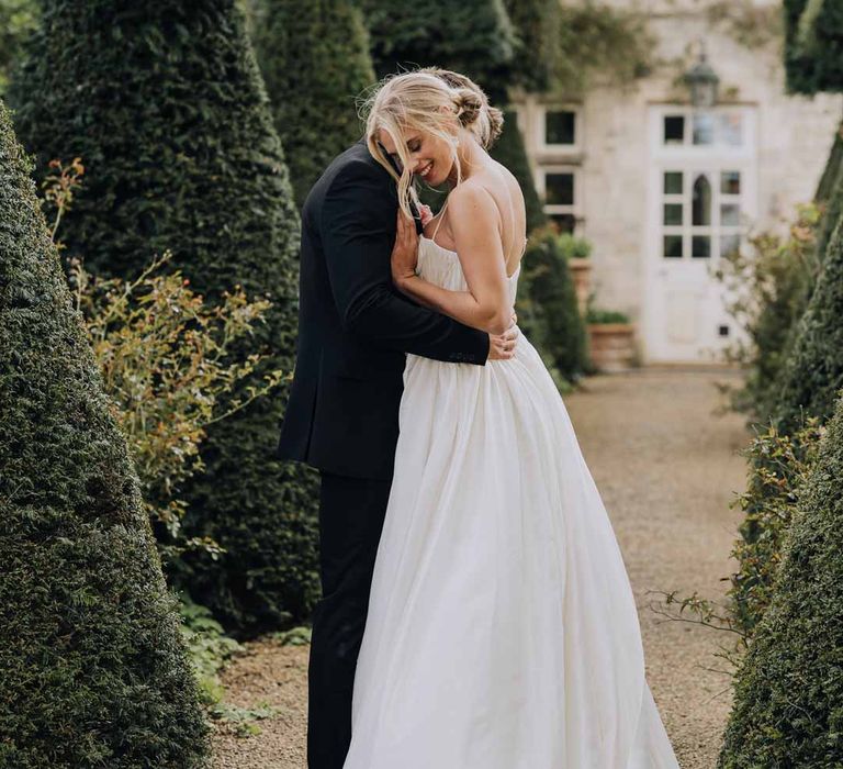 Bride in Watters strappy sleeveless princess wedding dress embracing groom in classic black tuxedo at Euridge Manor wedding venue