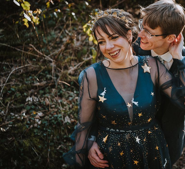 Bride in navy blue wedding dress with long sleeves and gold stars and matching crown with groom 