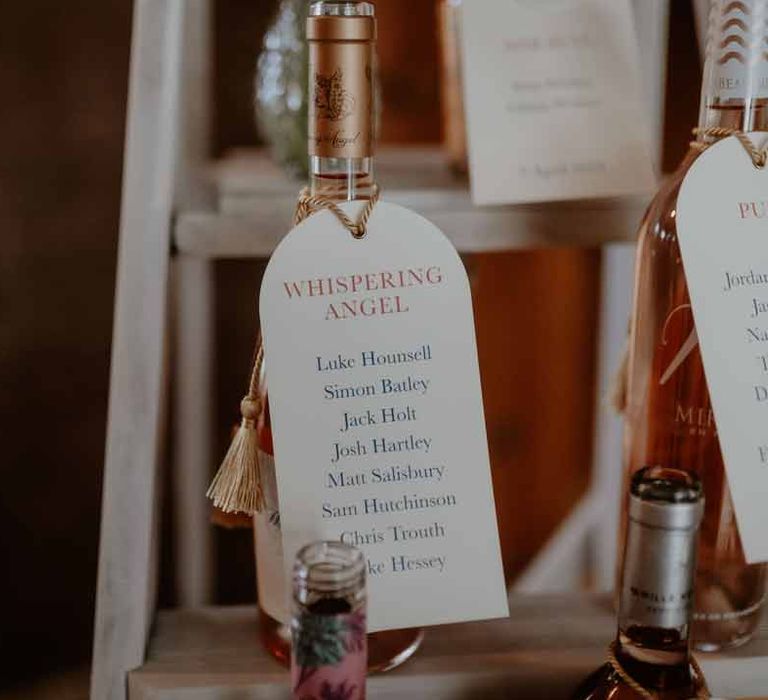 Rose-inspired wedding table numbers hung on the neck of a bottle of rose wine at Elmore Court Gloucestershire wedding