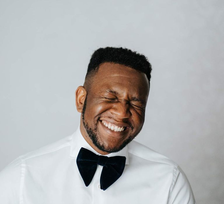 Groom laughing in crisp white shirt and black velvet bowtie 