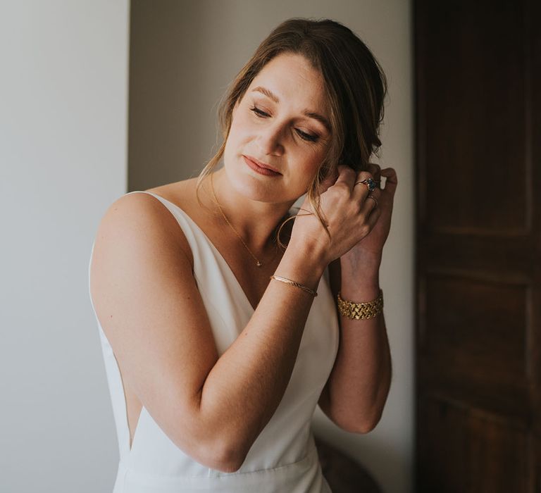 Bride in classic wedding dress putting on her Monica Vinader wedding earrings 