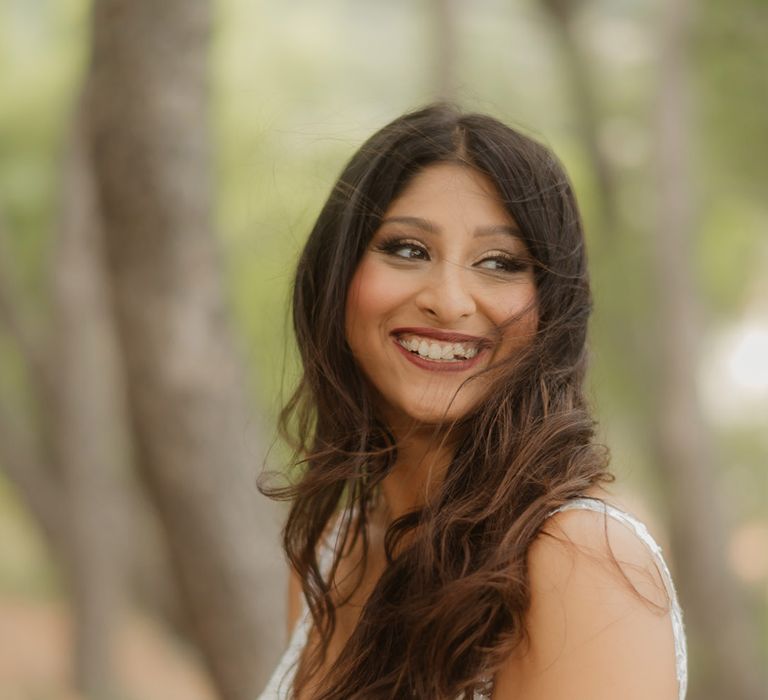 Indian bride with long wavy brown hair and deep red lipstick smiling 